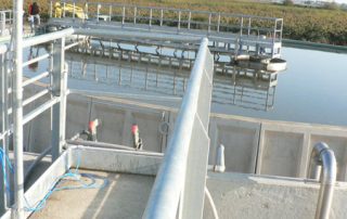 Passerella sopra una vasca industriale di trattamento delle acque, con corrimano e impianti tecnici installati.