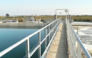 Passerella sopra una vasca industriale di trattamento delle acque, con corrimano e impianti tecnici installati.