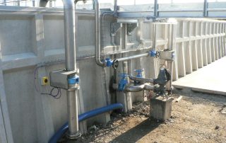 Impianto industriale con tubazioni in acciaio inox e valvole installate su una vasca prefabbricata in cemento.