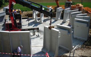 Costruzione di una vasca industriale con elementi prefabbricati in cemento, sollevati e posizionati da una gru.