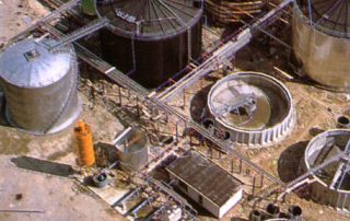 Vista aerea di un impianto di trattamento delle acque con vasche circolari e serbatoi metallici.