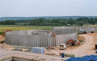 Impianto industriale in costruzione con grandi vasche circolari prefabbricate in cemento.