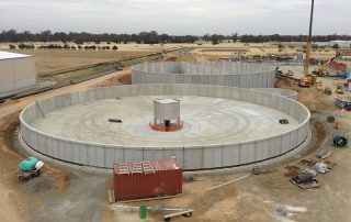 Impianto industriale in costruzione con grandi vasche circolari prefabbricate in cemento.