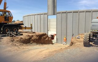 Costruzione di una vasca industriale in cemento con una gru che solleva un pannello prefabbricato per l’installazione.