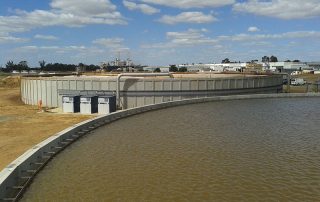 Grande vasca industriale in cemento contenente acqua, con un impianto di trattamento sullo sfondo.