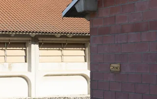 Una porcilaia in cemento con un tetto in tegole rosse. La struttura presenta finestre a lamelle regolabili per la ventilazione.