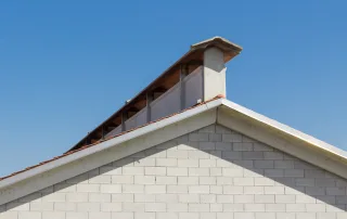 Primo piano del tetto di una porcilaia in muratura chiara, dotata di un sistema di ventilazione a camino rialzato in cemento.