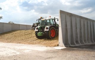 Trattori agricoli al lavoro su un silo per insilato, con pareti in cemento armato per il contenimento del materiale. La struttura rinforzata delle pareti assicura la stabilità del silo durante il processo di compattazione con i mezzi pesanti.