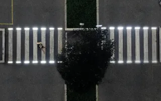 Attraversamento pedonale illuminato da luci a LED integrate nelle strisce bianche, visto dall'alto di notte.