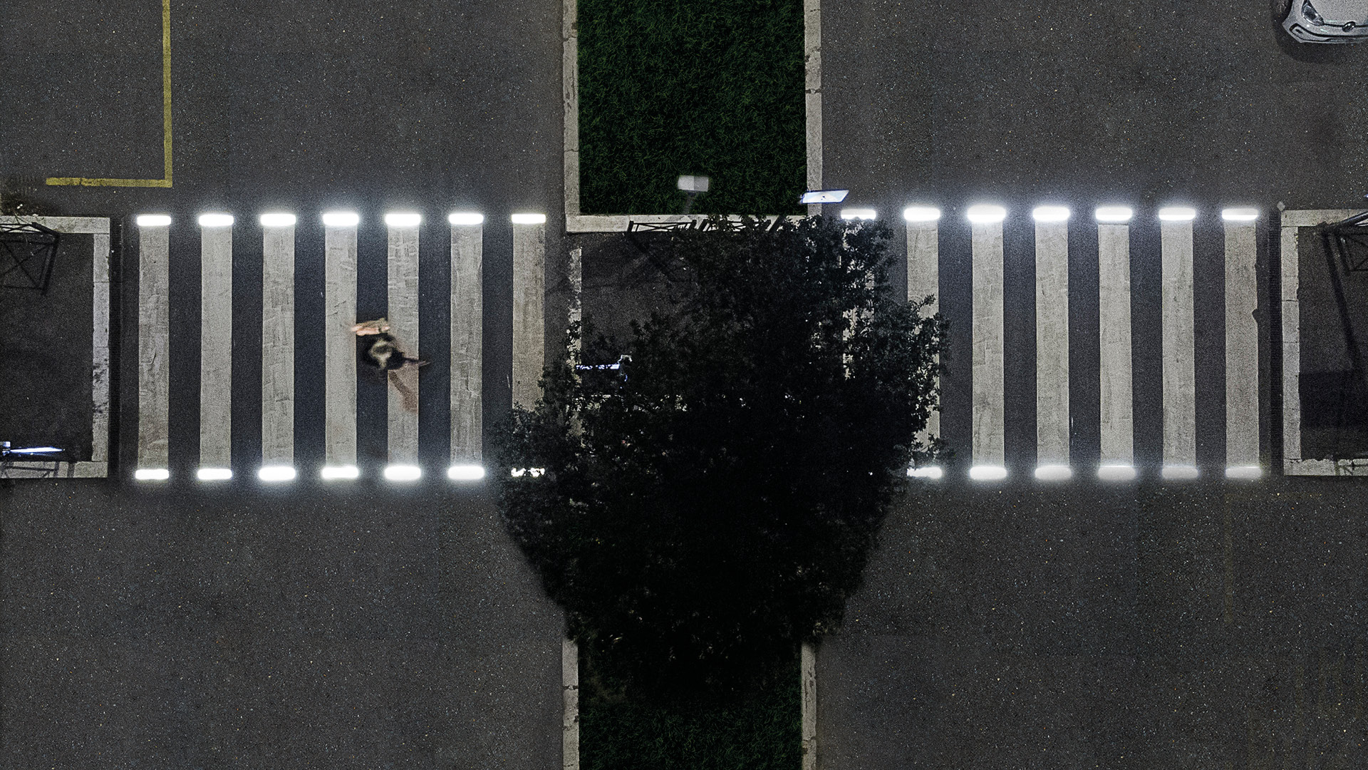 Attraversamento pedonale illuminato da luci a LED integrate nelle strisce bianche, visto dall'alto di notte.