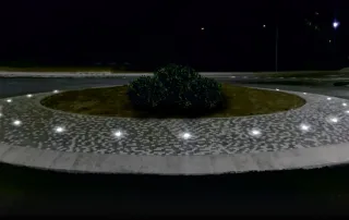 Illuminazione a LED integrata in una rotatoria stradale. Piccoli punti luce bianchi sono posizionati lungo il bordo del marciapiede.