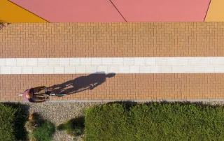 Marciapiede pavimentato con blocchi rettangolari marroni con una fascia centrale bianca.