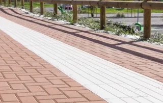 Marciapiede pavimentato con blocchi rettangolari rossi con una fascia centrale bianca.