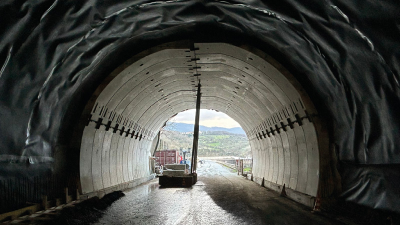 Interno di un tunnel in costruzione, con pareti rivestite da segmenti prefabbricati in calcestruzzo. Le pareti laterali mostrano segmenti già fissati, mentre nella parte superiore è visibile una sezione ancora aperta.