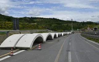 antiere stradale con elementi prefabbricati in calcestruzzo posizionati lungo la carreggiata, destinati al rivestimento della galleria in costruzione. Coni stradali segnalano l'area di lavoro.