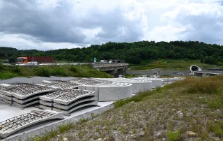 Zona di cantiere con elementi prefabbricati in calcestruzzo e armature metalliche accatastate, destinate al rivestimento di una galleria.