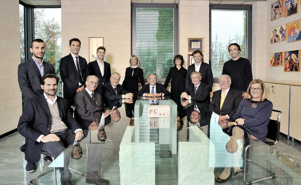 Foto di gruppo del team dirigenziale di Paver all'interno di una sala riunioni con un tavolo di vetro. Dodici persone tra uomini e donne in abbigliamento formale e semi-formale, sorridenti. Sul tavolo è presente un blocco con la scritta 'PC SPA'. L'ambiente ha grandi finestre e pareti con quadri colorati.