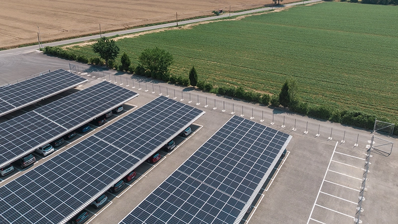 Parcheggio con pensiline fotovoltaiche in cemento dotate di pannelli solari, situato in un'area aperta.