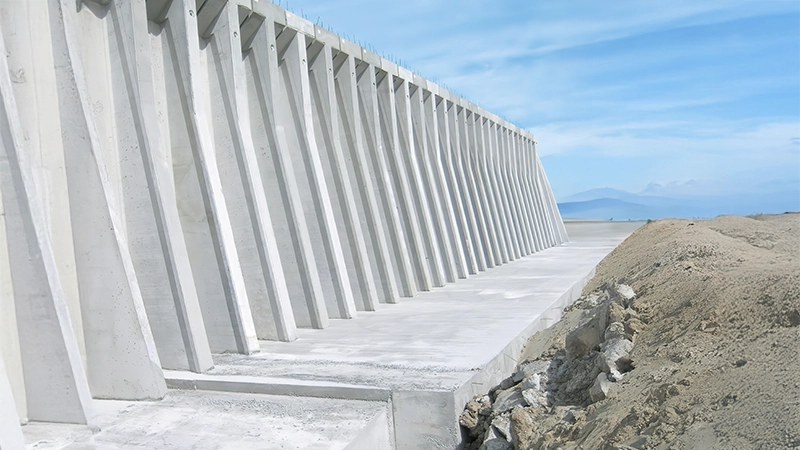 Muro di sostegno in calcestruzzo armato con elementi inclinati, realizzato per contenere il terreno in un'area infrastrutturale aperta.