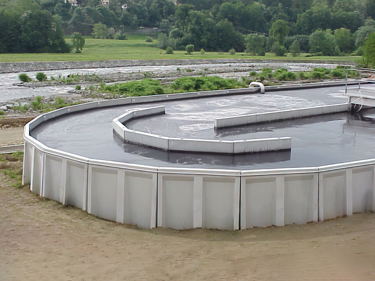 Una grande vasca industriale di forma rettangolare. La vasca contiene un liquido scuro e denso.